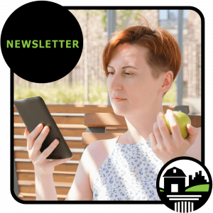 woman with short red hair reads tablet and eats apple on park bench
